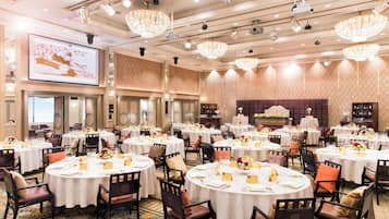 A banquet hall with round tables, chairs, and chandeliers.