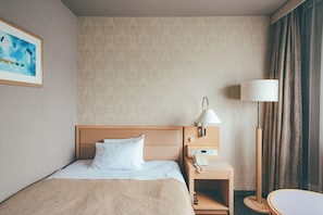 A hotel room with a bed, a bedside table with a lamp, a phone, and a painting on the wall. - Numazu Riverside Hotel (Numazu)