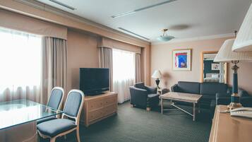 A hotel room with a television, two armchairs, a sofa, a small table, and a lamp.