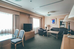 A hotel room with a television, two armchairs, a sofa, a small table, and a lamp.
