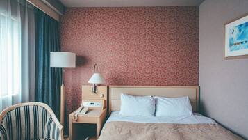 Una habitación de hotel con una cama, una silla, una mesita de noche con lámpara y un cuadro en la pared.