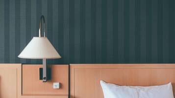 A hotel room with a bed, a nightstand, a lamp, and a wall socket.