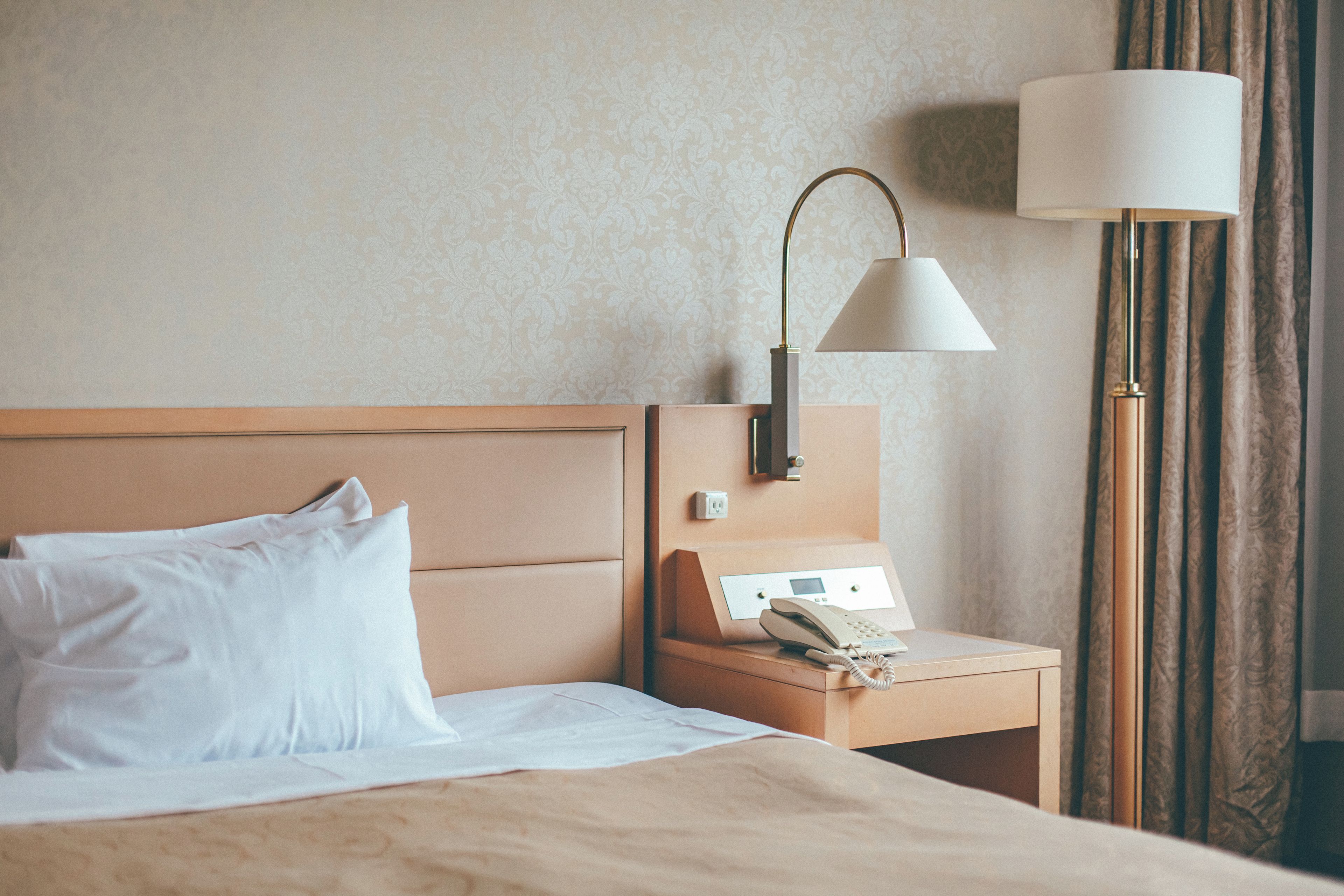 A hotel room with a bed, a nightstand with a lamp, and a telephone.