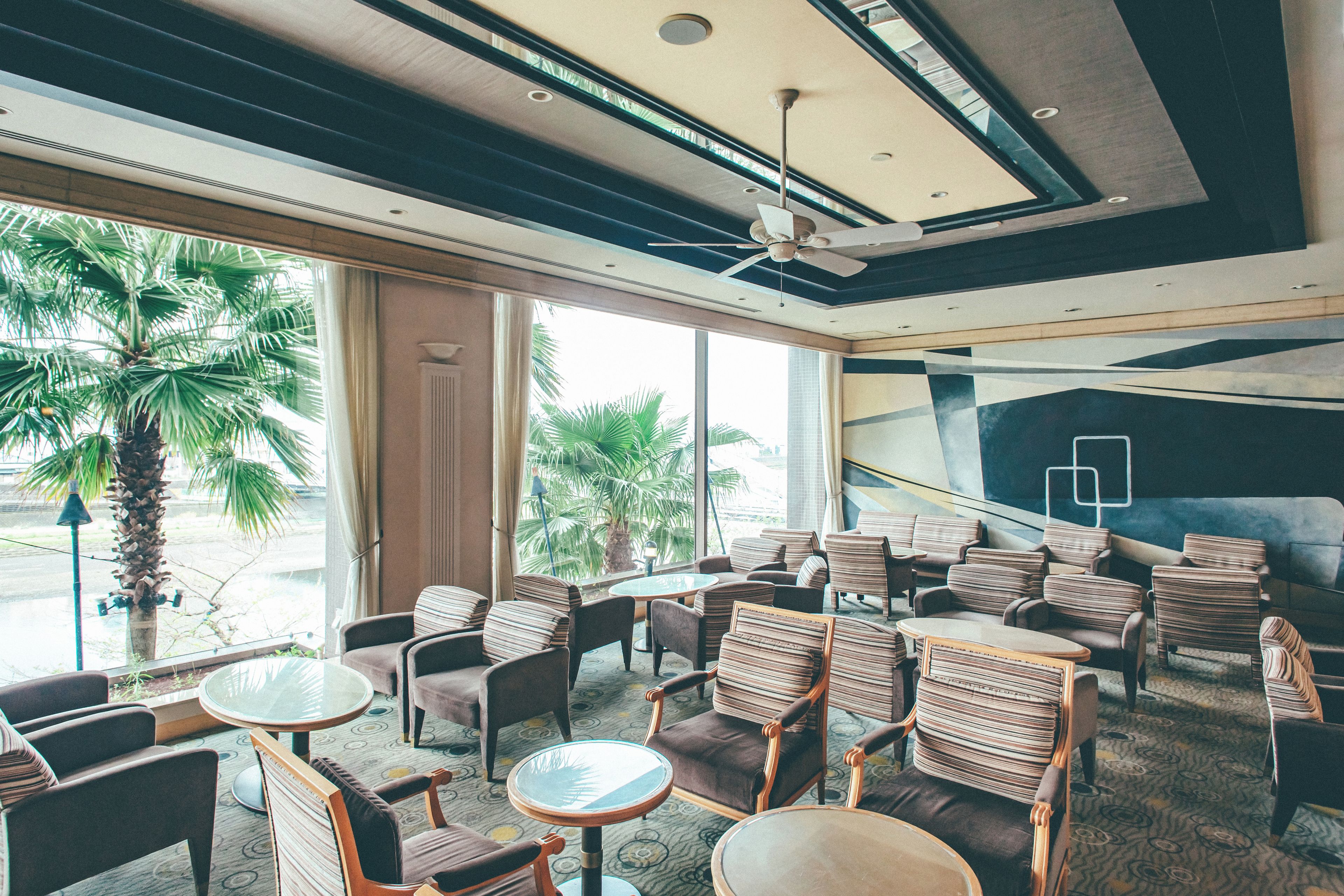 A hotel lobby with seating areas, large windows, and a ceiling fan.