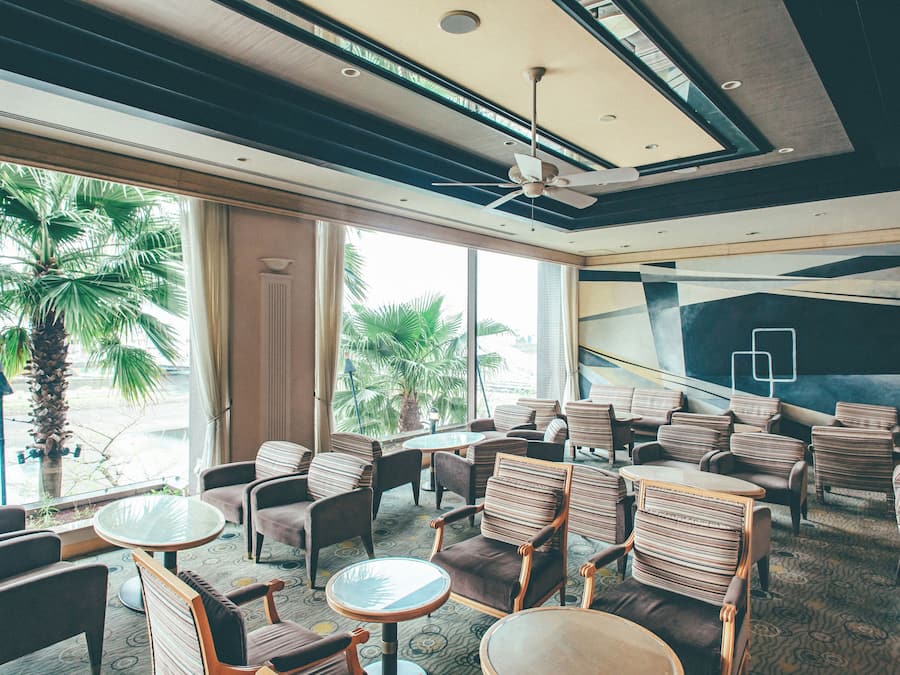 Un vestíbulo de hotel con zonas de estar, ventanas amplias y un ventilador de techo.