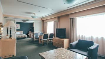 Habitación de hotel con cama, escritorio, sillas, televisor y un ventanal con cortinas.
