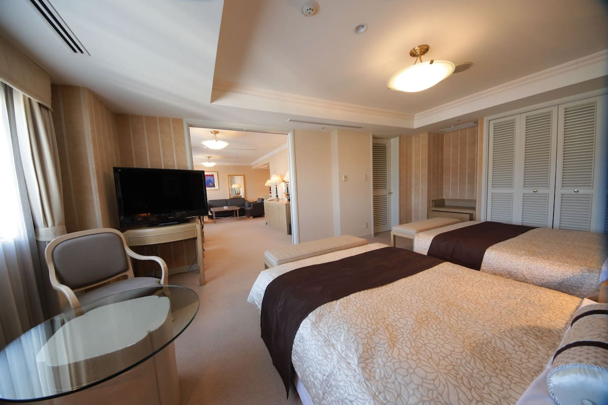 A hotel room with two beds, a TV, a desk, and a glass table.