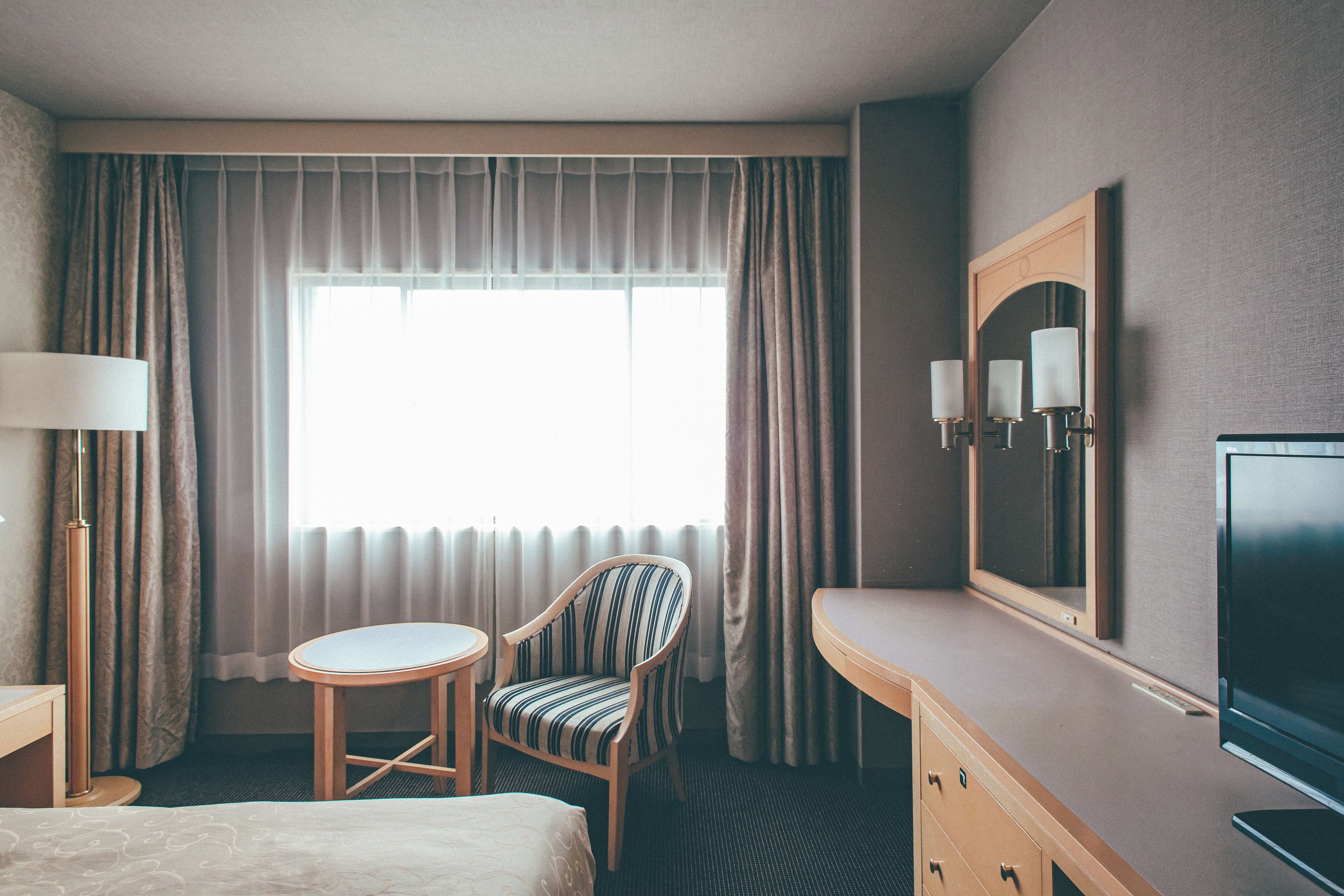 A hotel room with a bed, a chair, a desk, a television, and a large window with curtains.