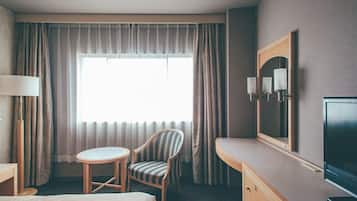 A hotel room with a bed, a chair, a desk, a television, and a large window with curtains.