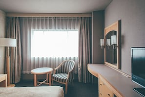 A hotel room with a bed, a chair, a desk, a television, and a large window with curtains.