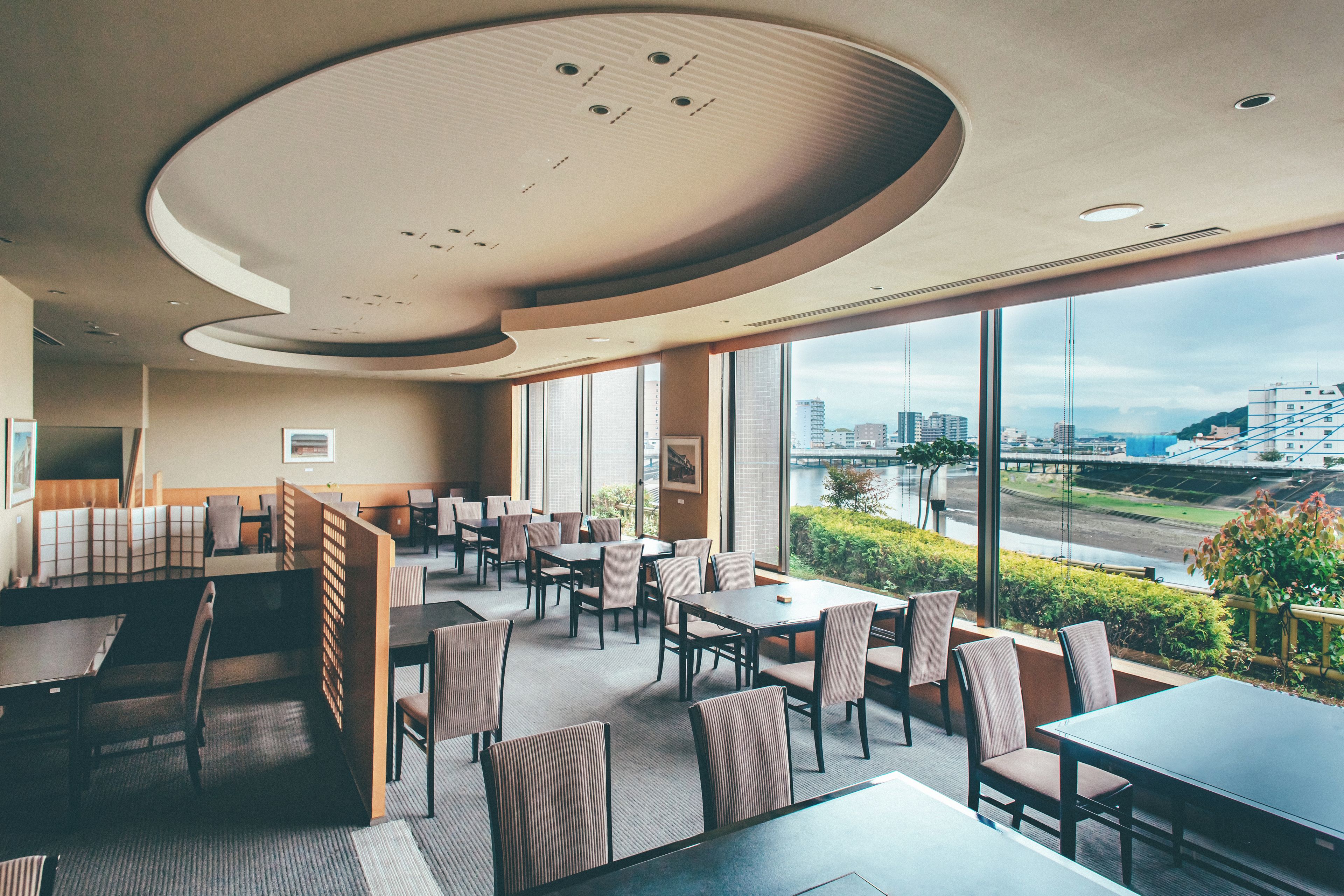 A modern restaurant with high ceilings, large windows, and a view of a cityscape.