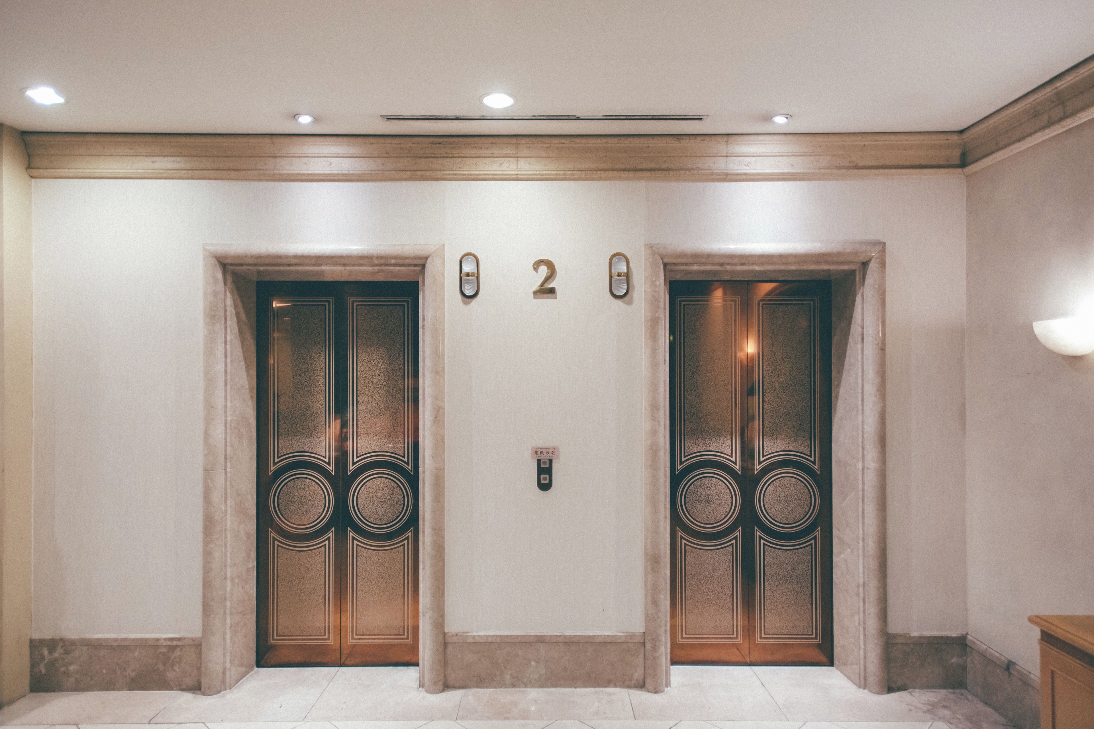 A hallway with two elevator doors, each with a number plate and a doorbell.