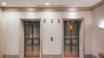 A hallway with two elevator doors, each with a number plate and a doorbell.