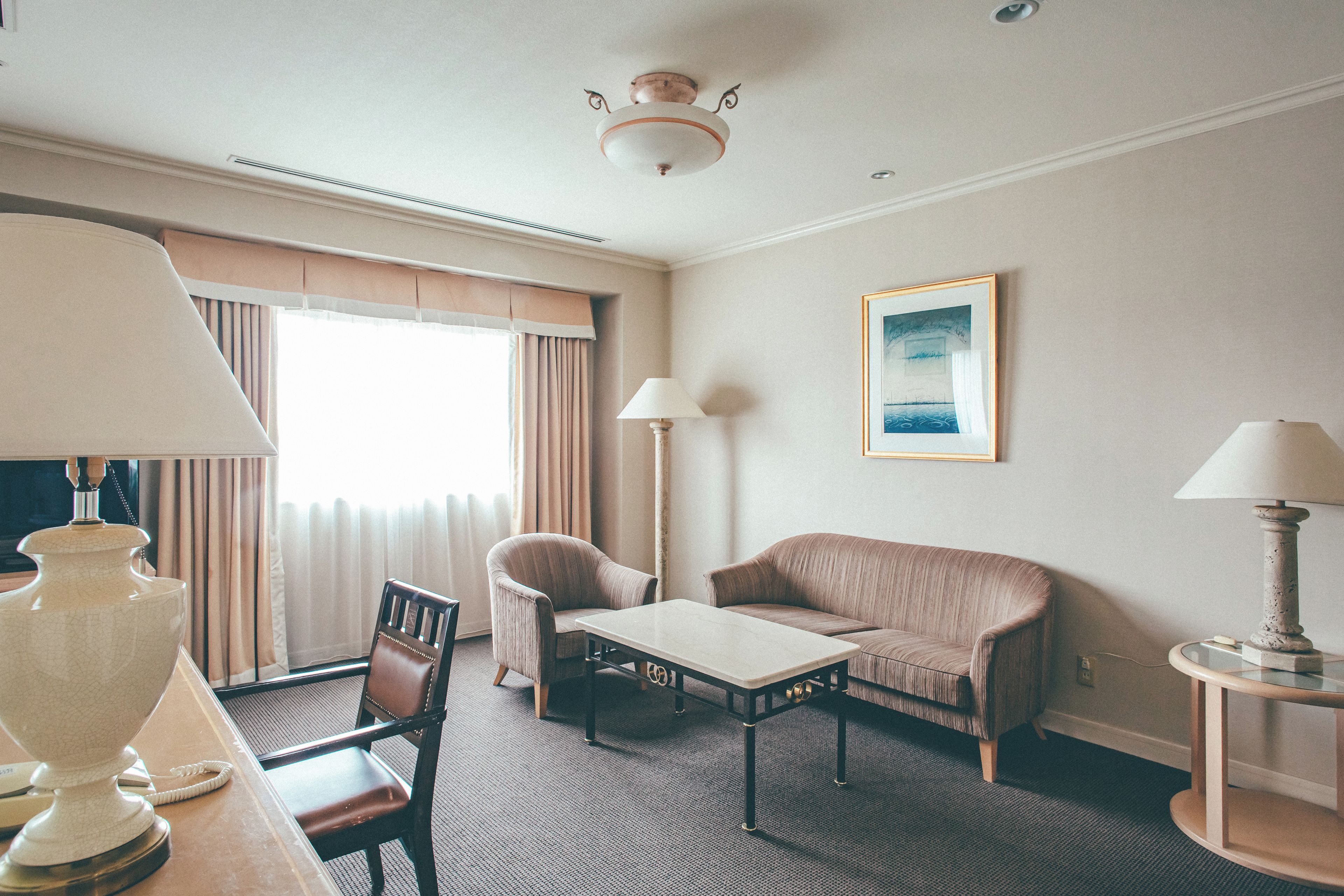 A hotel room with a bed, a desk, a chair, a sofa, a lamp, and a painting on the wall.