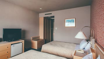 A hotel room with two beds, a desk with a television, a lamp, and a small refrigerator.
