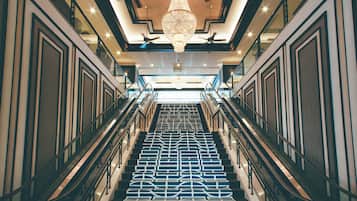 A grand staircase with a geometric patterned floor, flanked by glass railings and a central chandelier.