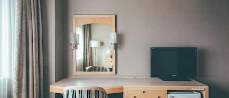 A hotel room with a desk, a television, a mirror, and a wardrobe.