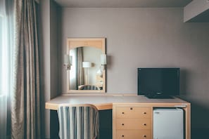 A hotel room with a desk, a television, a mirror, and a wardrobe.