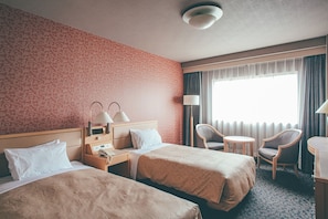 Et hotelværelse med to senge, et skrivebord, en stol, en lampe og et vindue med gardiner.