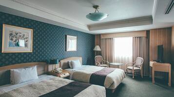 A hotel room with two beds, a desk, a chair, a lamp, and a television.