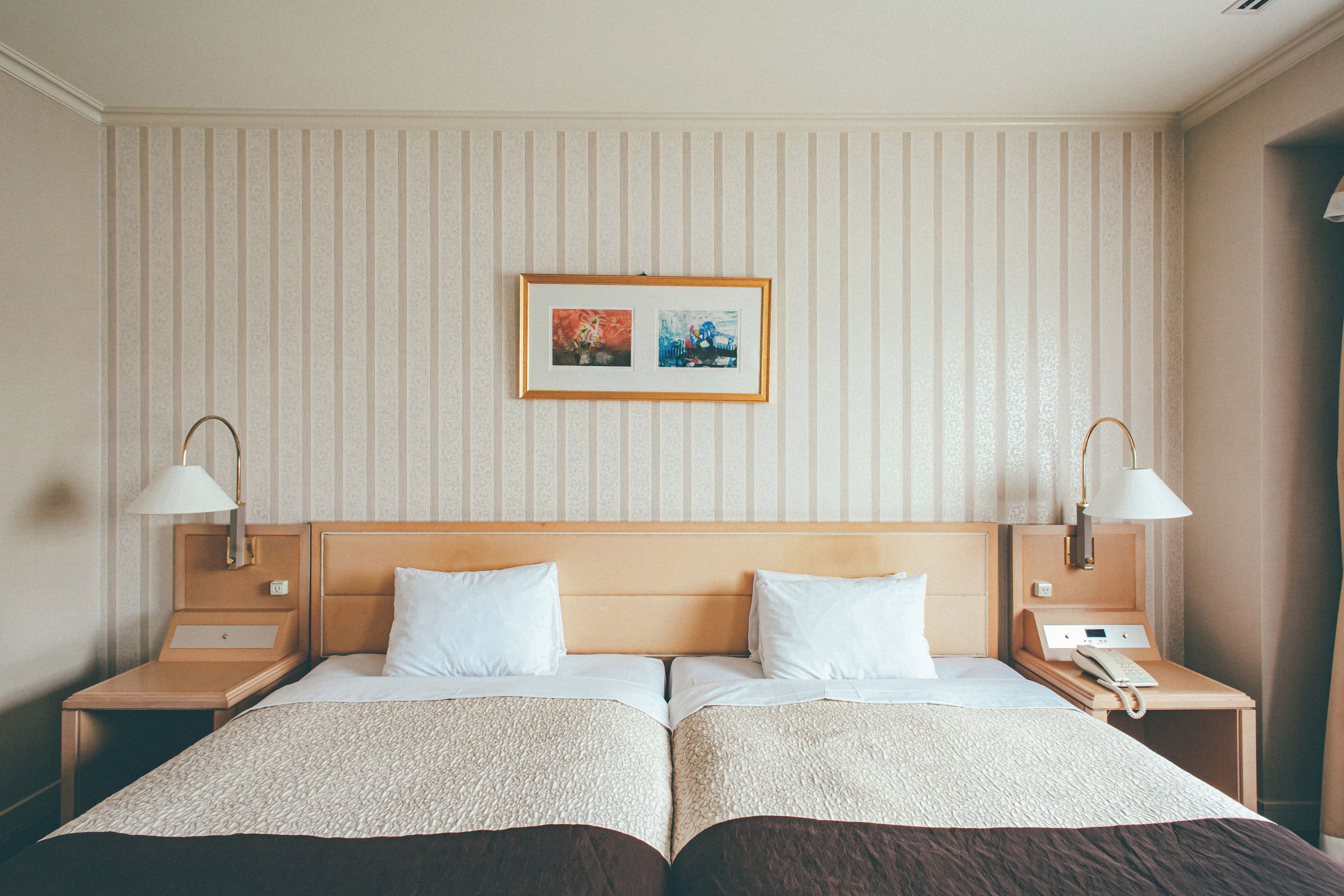 A hotel room with two beds, a headboard, bedside lamps, and a framed picture on the wall.