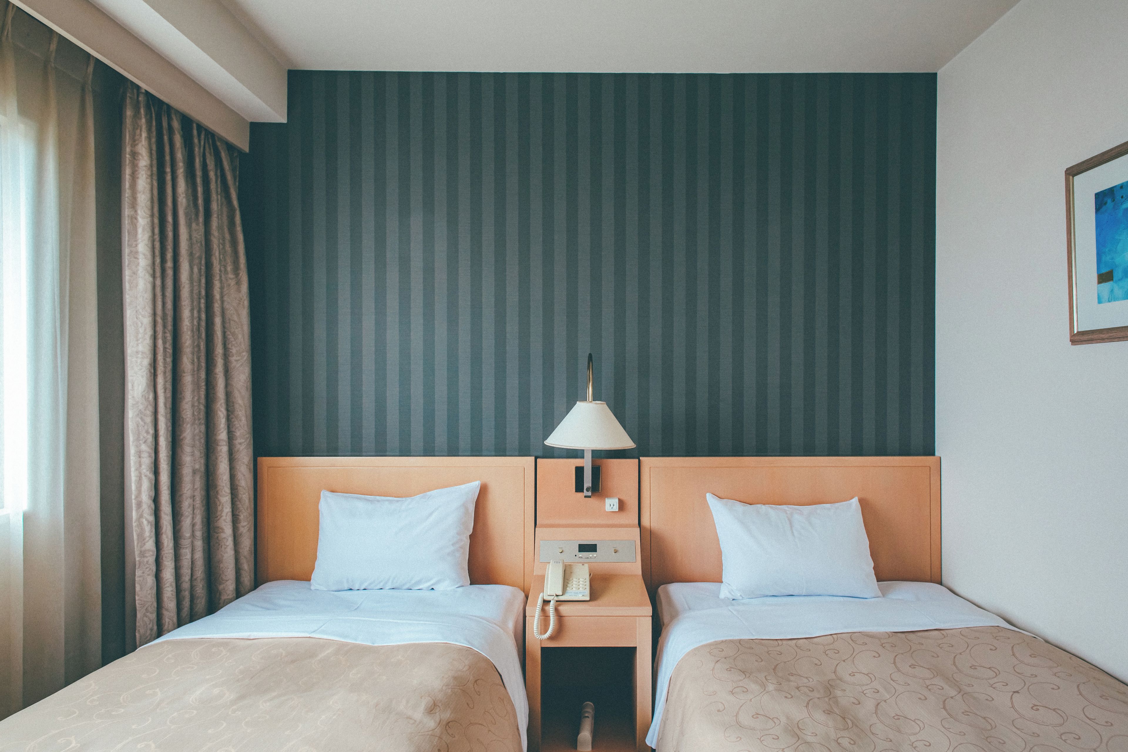A hotel room with two beds, a nightstand with a lamp, and a painting on the wall.