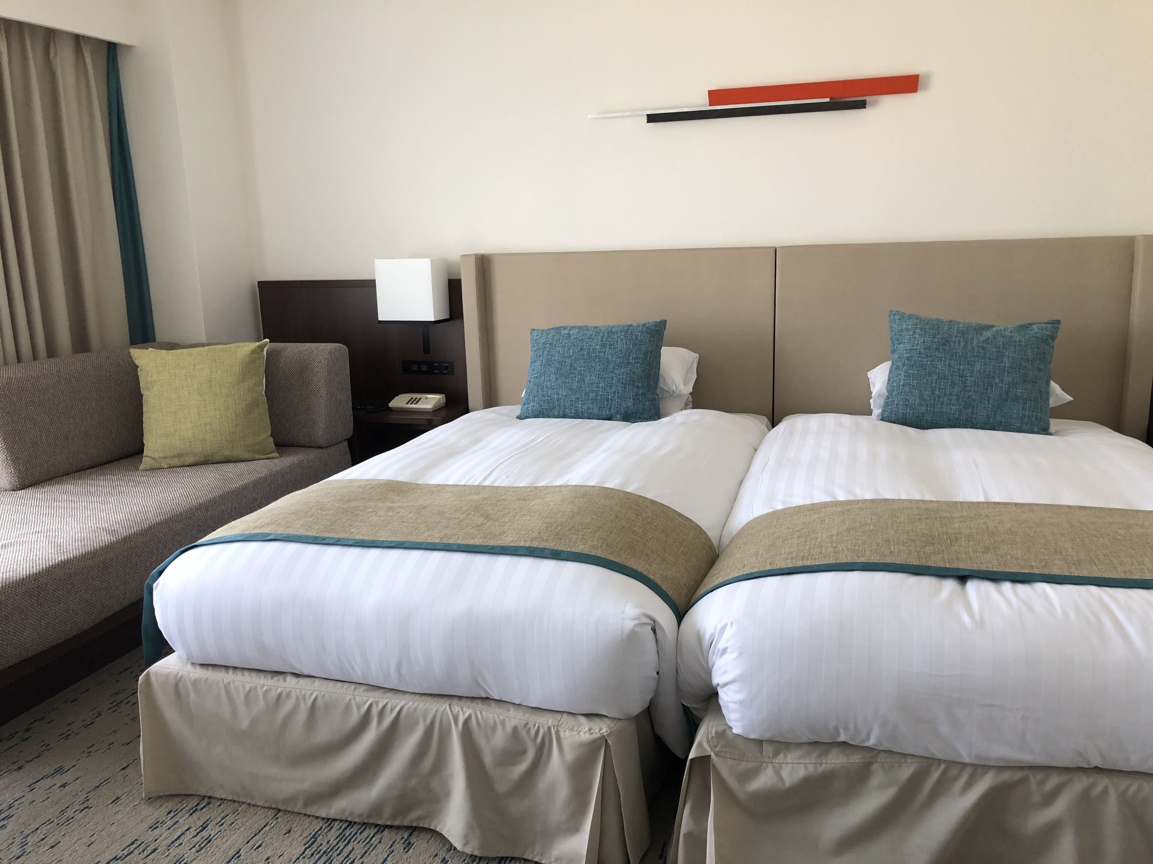 A hotel room with two beds, a sofa, a nightstand, and a lamp.