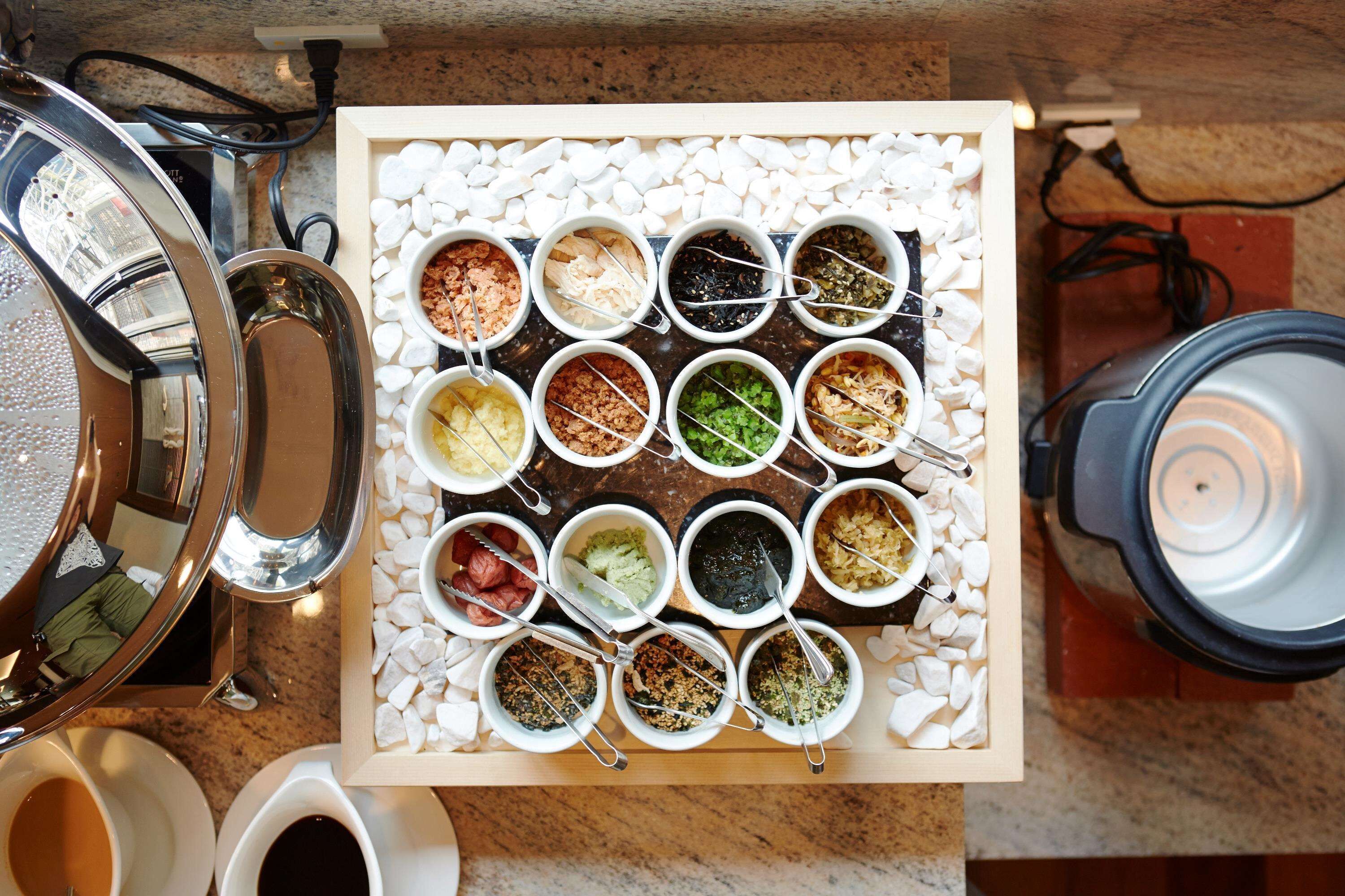 A buffet setup with various food items in bowls on a tray, a coffee machine, and a tea kettle.