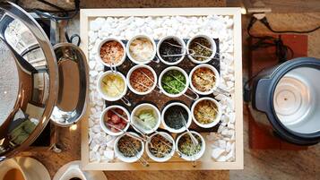 A buffet setup with various food items in bowls on a tray, a coffee machine, and a tea kettle.