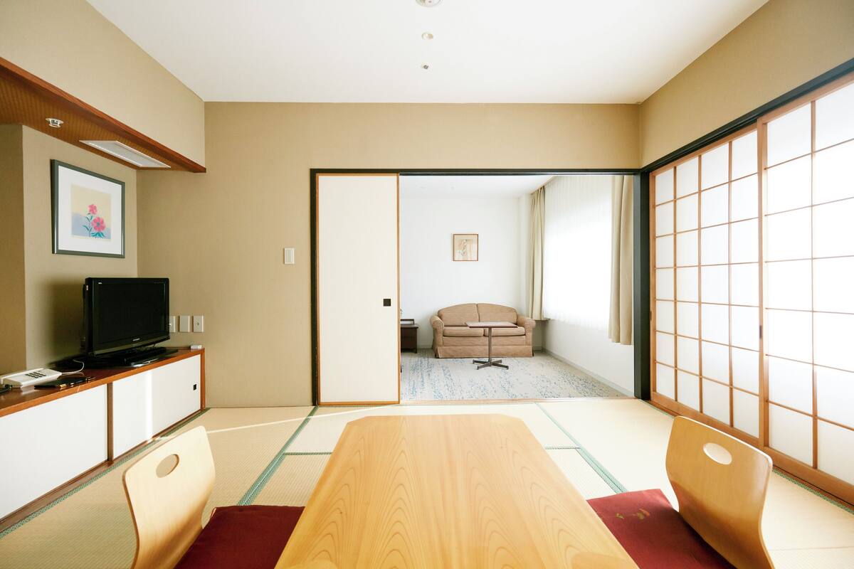 A traditional Japanese room with tatami flooring, a low table, and a television on a cabinet.