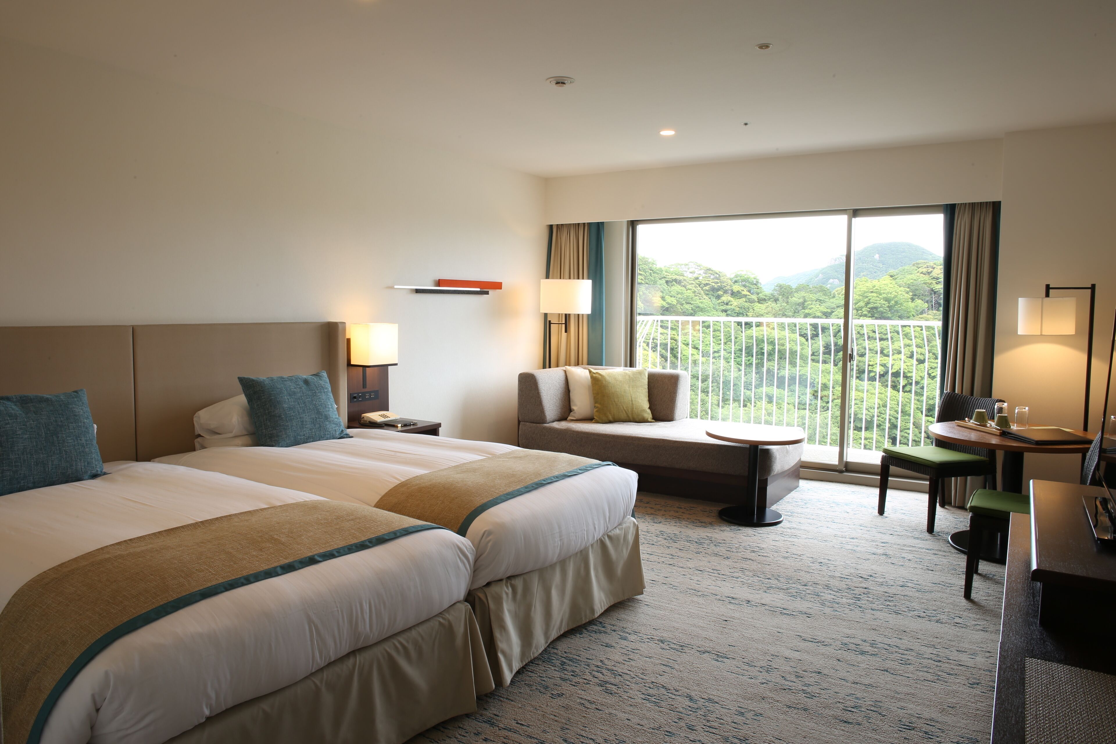 A hotel room with two beds, a sofa, a balcony with a view, and a desk with a chair.