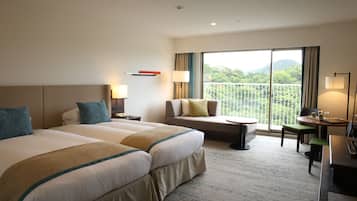 A hotel room with two beds, a sofa, a balcony with a view, and a desk with a chair.