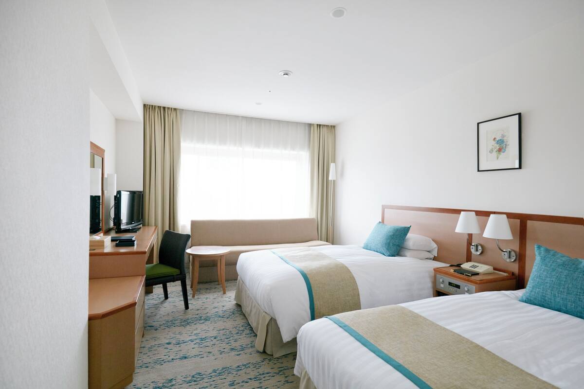 A hotel room with two beds, a desk with a television, a chair, and a small table.