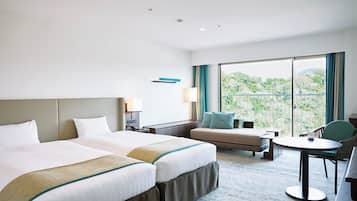 Habitación de hotel con dos camas, un sofá, una mesita y un balcón con vistas a la vegetación.