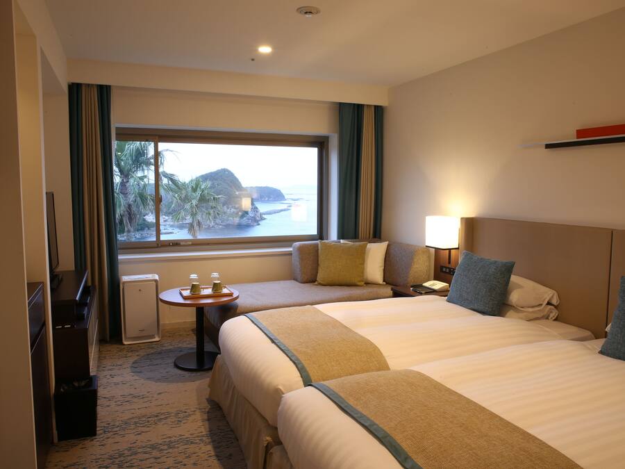 A hotel room with two beds, a view of the sea, a small table with a lamp, and a TV.