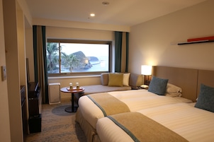 Habitación de hotel con dos camas, vista al mar, una mesita con lámpara y televisión.