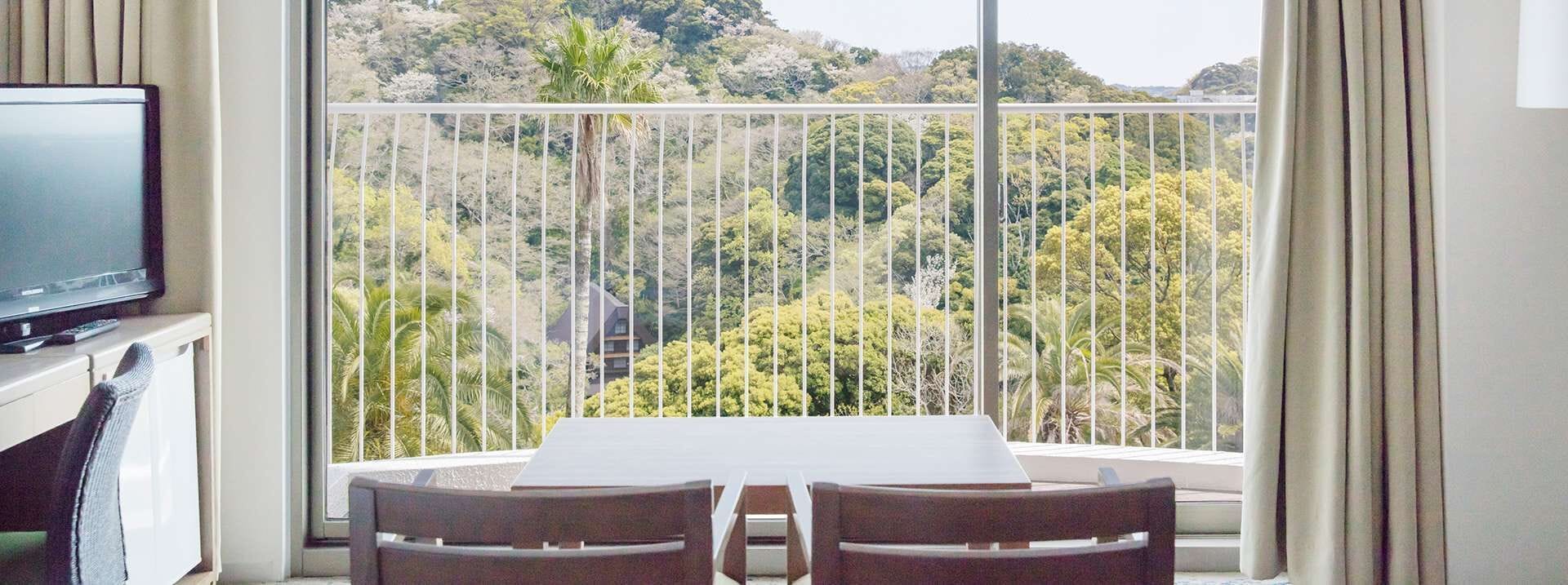 En balkon med et bord, stole, et fjernsyn og udsigt til et skovområde.