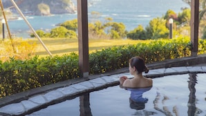 Una persona de pie junto a una piscina con vista al océano y una montaña al fondo.
