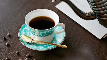 A cup of coffee on a saucer with a spoon, surrounded by coffee beans on a wooden table.