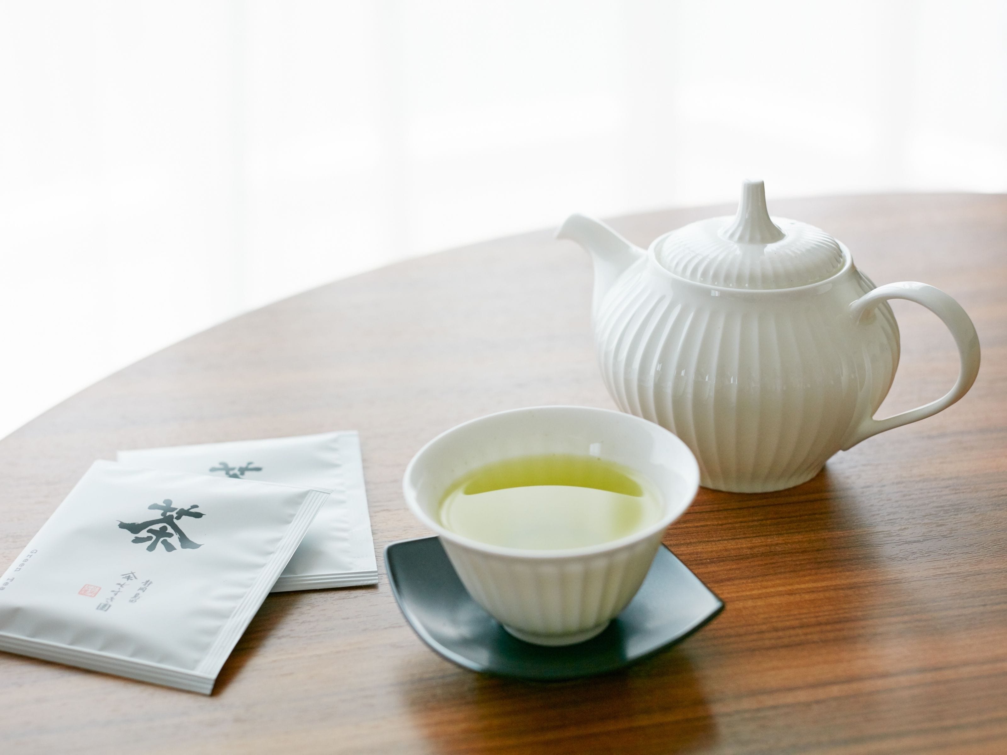 Una tetera blanca y una taza de té sobre una mesa de madera, con una servilleta y una bolsita de té a su lado.