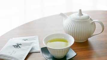 Una tetera blanca y una taza de té sobre una mesa de madera, con una servilleta y una bolsita de té a su lado.
