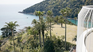 Vista costera con palmeras, una playa y montañas al fondo.