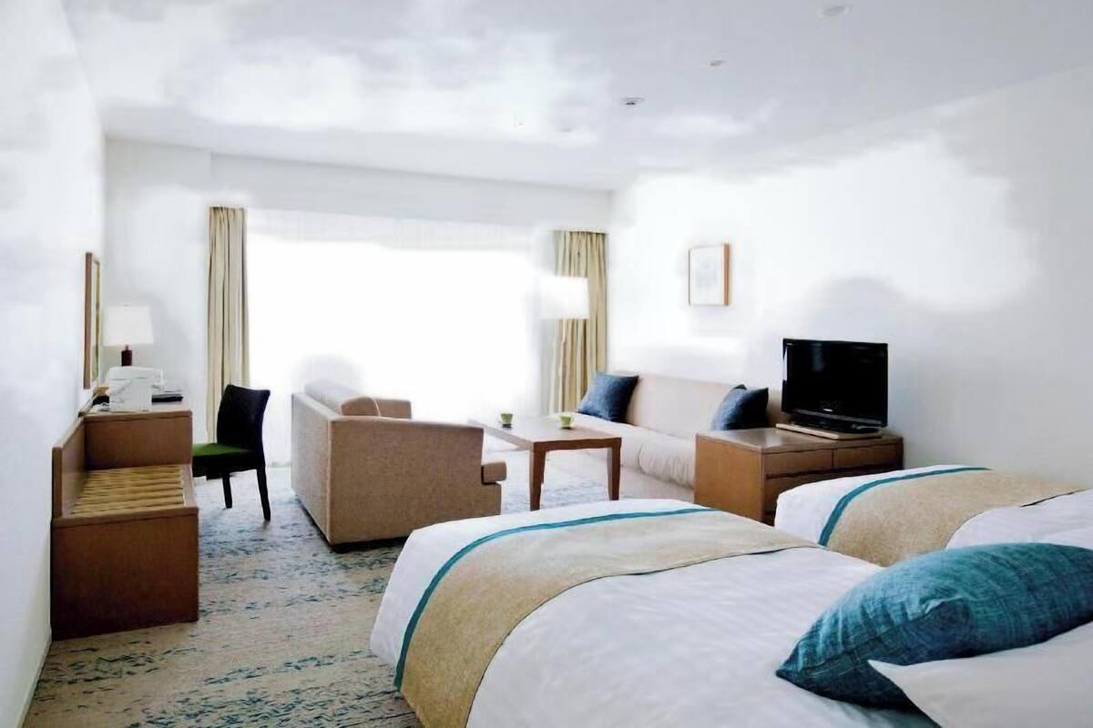 A hotel room with two beds, a sofa, a TV, a desk, and a lamp.