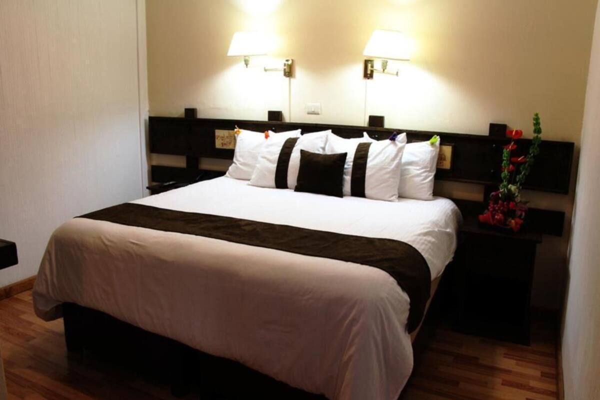 A hotel room with a large bed, two bedside tables, and two wall-mounted lamps.