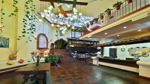A spacious lobby with a central staircase, potted plants, and a tiled floor.