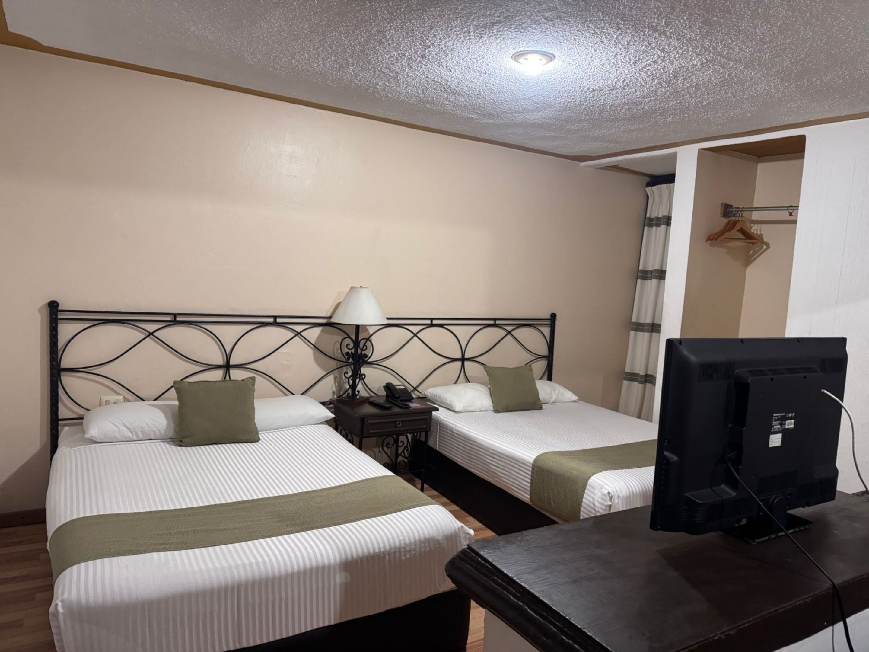 A hotel room with two single beds, a desk with a television, and a small table with a lamp.