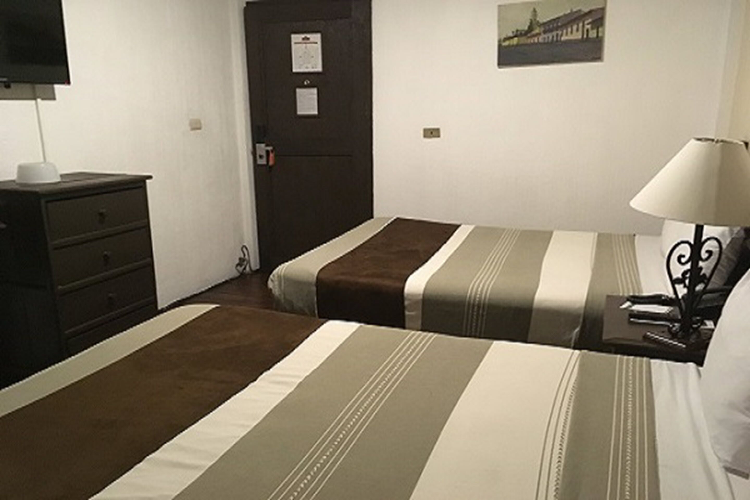 Habitación de hotel con dos camas, un aparador, una lámpara y una puerta con un aviso.