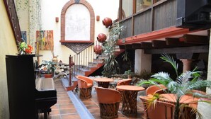 An outdoor patio area with a piano, wicker chairs, terracotta pots, and a tiled floor.