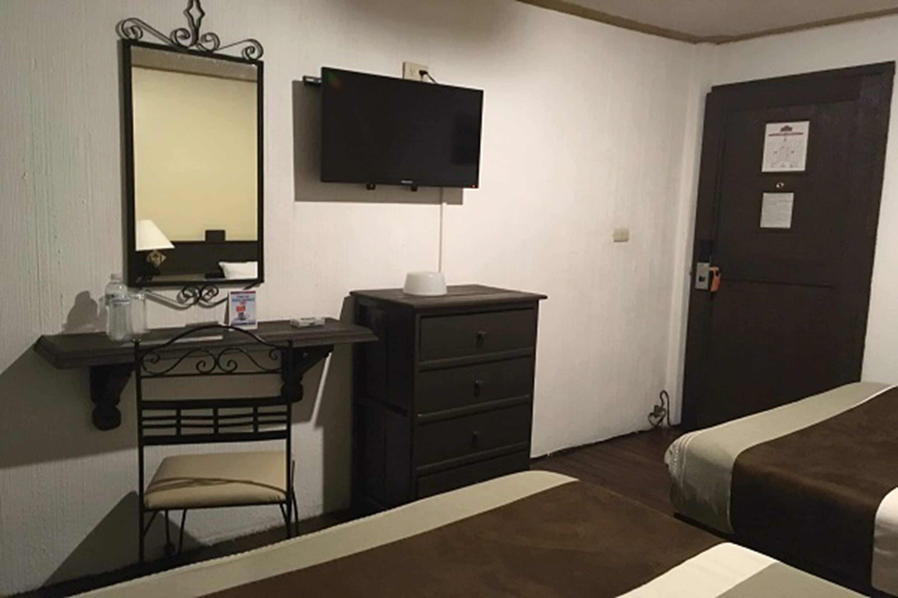Una habitación de hotel con una cama, un escritorio con una silla, un televisor y un armario.