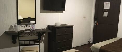 Una habitación de hotel con una cama, un escritorio con una silla, un televisor y un armario.